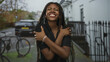 © Krakenimages.com - Woman smiling with arms crossed hugging herself on a residential city street by parked bicycles and iron railings; self love joy.