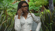 © Krakenimages.com - African american woman holding smartphone to ear and touching chest in forest walkway, wearing glasses and braided hair in white shirt; concern focus.
