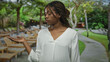 © Krakenimages.com - African american woman holding palm up with open hand on a street lined with lounge chairs and trees; contemplation.