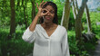 © Krakenimages.com - Woman makes ok gesture with fingers around one eye in a forest park wearing a white blouse; playful curiosity.