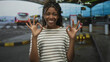 © Krakenimages.com - Woman in striped top smiling and making ok sign with both hands at airport terminal curbside pickup; friendly joy.