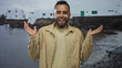 © Krakenimages.com - Man smiling with face visible and raised hands by rocky seaside building near shore, wearing checked shirt and necklace while looking toward camera; carefree joy.