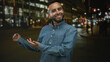 © Krakenimages.com - Young man with beard wearing denim shirt showing open hands and smiling on a busy city street at night; confidence.
