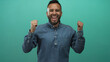 © Krakenimages.com - Young hispanic man wearing denim shirt shouting with hand cupped to mouth in teal studio; joy energy.