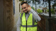 © Krakenimages.com - Man engineer makes phone gesture with hand on street wearing yellow reflective vest; friendly professionalism.