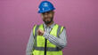 © Krakenimages.com - Man engineer wearing blue hardhat and neon safety vest smiles and taps wrist in pink studio; safety awareness confident readiness.