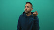 © Krakenimages.com - Man raising his fist in studio against a teal wall wearing a navy hoodie and visible beard; defiance doubt.