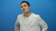 © Krakenimages.com - Young man with a white shirt stands confidently against a vibrant blue wall, showcasing a relaxed and thoughtful expression.