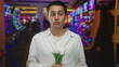 © Krakenimages.com - Young man in a casino holding flowers indoors near vibrant slot machines offers a blend of emotion and culture against the colorful background of a bustling gaming environment.