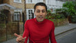 © Krakenimages.com - Young man with short hair in red shirt gesturing on a quiet urban street with brick houses and green foliage visible in the background.