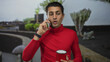 © Krakenimages.com - Young man in a red shirt holding a coffee cup and talking on a cellphone outdoors with cacti in the background, exuding casual confidence in a vibrant setting.