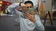 © Krakenimages.com - Young hispanic man displaying australian banknotes on an urban street, showcasing wealth and financial success against a lively city backdrop.
