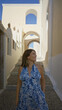 © Krakenimages.com - Woman in blue floral dress smiling and looking up on santorini street with arched white buildings; travel serenity.