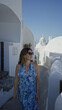 © Krakenimages.com - Woman walking on a narrow santorini street in a blue floral halter dress and sunglasses, strolling past white domes and walls; serenity wanderlust holiday.
