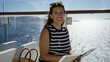 © Krakenimages.com - Woman gestures with hand while reading a book on a terrace building by the ocean railing; serenity leisure travel.