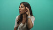 © Krakenimages.com - Young woman cupping her ear with a hand in teal studio wall setting wearing bracelets; curiosity listening focus.