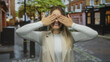 © Krakenimages.com - Woman smiling playfully covering her eyes in a vibrant city street setting, exuding joy and a carefree attitude, captured outdoors in an urban environment for a fun lifestyle concept.