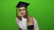 © Krakenimages.com - Young woman with book and graduation cap stands against green wall, appearing thoughtful and contemplative