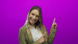 © Krakenimages.com - Smiling woman pointing upward in front of a vibrant purple background, showcasing her blonde hair and cheerful demeanor.