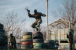 © qunica.com - A masked performer leaps mid-air over stacked tires during an outdoor obstacle course. Soldiers in camouflage observe from the background.