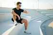 © muse studio - Man sits on steps and checks watch while wearing sports gear in outdoor setting during daylight hours