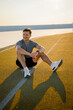 © muse studio - Man sits on running track during sunset after training in sportswear near a stadium