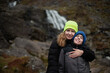 © Мар'ян Філь - Mother and young son embrace and smile, talk during an outdoor hike beside rocky waterfall, wearing warm beanies and jackets. A candid, affectionate family moment
