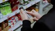 © Alexander - Customer is reading the nutritional information and ingredients on a bottle of dressing while shopping in a grocery store. A customer in black studies the label on a bottle of sauce