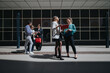 © qunica.com - A group of business colleagues stand outside a modern office building reviewing documents and folders. Two women and three coworkers engage in a casual meeting and conversation on the plaza.