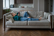 © ingoodtime - Relaxed woman using phone lying on couch at home. Interested female scrolling webs, watching video, online shopping on smartphone spending screen time with internet services lounging in living room.