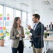 © Jay - Dynamic Dialogue: Two business professionals engage in a focused discussion in a modern office environment, with a backdrop of collaborative workspace and creative ideas.