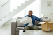 © Wavebreak Media - African American man sitting at home on sofa holding white box beside shipping box with smartphone