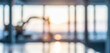 © al-sultan - Blurred background of a modern workspace with large windows capturing a soft sunset glow. Industrial machinery visible in the distance, adding context to the setting.