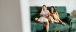 © Alberto - Women friends sharing a fun moment gaming at home, relaxing on a green sofa