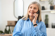 © New Africa - Smiling senior businesswoman talking by smartphone in office