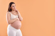 © New Africa - Choosing name for baby. Thoughtful pregnant woman on orange background, space for text