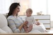 © New Africa - Smiling mother with her cute baby on sofa at home