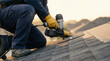 © ViskBx - Roofer installing new asphalt shingles with a nail gun on a residential house roof at sunset, closeup of the worker
