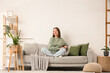 © Pixel-Shot - Happy young woman sitting on grey sofa in living room