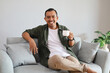 © ArvStd - A happy man holds a cup of coffee while relaxing on the sofa at home, smiling at the camera.