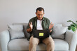 © ArvStd - An adult man sits on a sofa, reacting to bad news, looking at a laptop, raising his hands in shock, anger, questioning, disbelief at what he sees on the laptop.