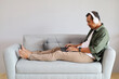 © ArvStd - A man relaxes sitting on the sofa at home, listening to music on his laptop with wireless headphones, nodding along to the beat, enjoying his favorite songs while working.