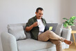 © ArvStd - A man sits comfortably on a sofa working on his laptop while enjoying a cup of coffee, looking relaxed and focused.