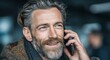 © MKS - The mature businessman with gray hair smiles as he uses a handheld electronic device within a modern office environment