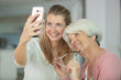 © auremar - senior mother and daughter taking selfie having fun at home