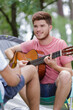 © auremar - young man playing guitar sat outside his tent