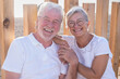 © luciano - A beautiful senior couple smiles carefreely sitting outdoors in the sunset light looking towards the camera, two cheerful pensioners standing together expressing love and serenity