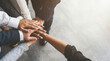 © Jonathan - A close-up overhead view of a diverse team's hands stacked together in a gesture of unity, collaboration, and support.