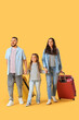 © Pixel-Shot - Family of travelers with suitcases walking on yellow background