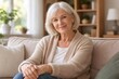 © Татьяна Евдокимова - Calm senior woman with white hair sitting comfortably on a beige sofa, enjoying a relaxed moment at home and looking directly at the camera with a friendly expression